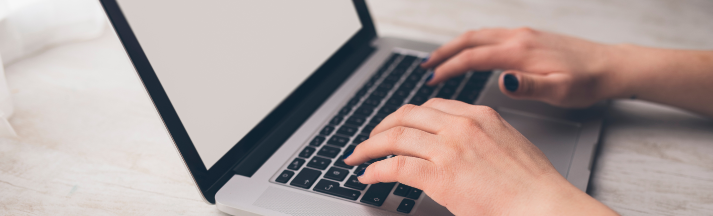 Et par kvinde hænder med sort neglelak skriver på et tastatur på en bærbar computer
