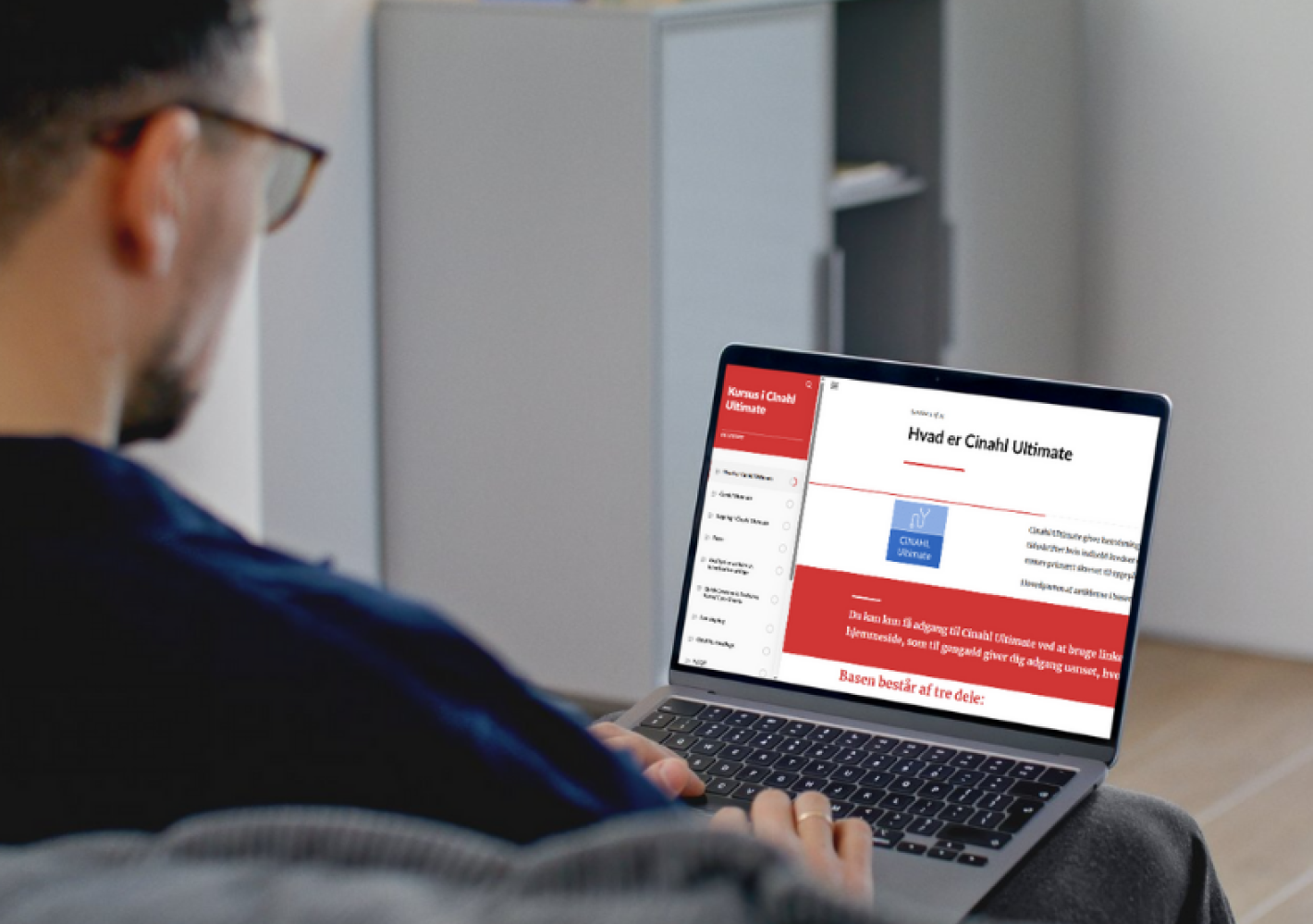 En person sidder i en sofa og ser på en bærbar computer, hvor der er åbnet et Rise360 modul om "Cinahl Ultimate"