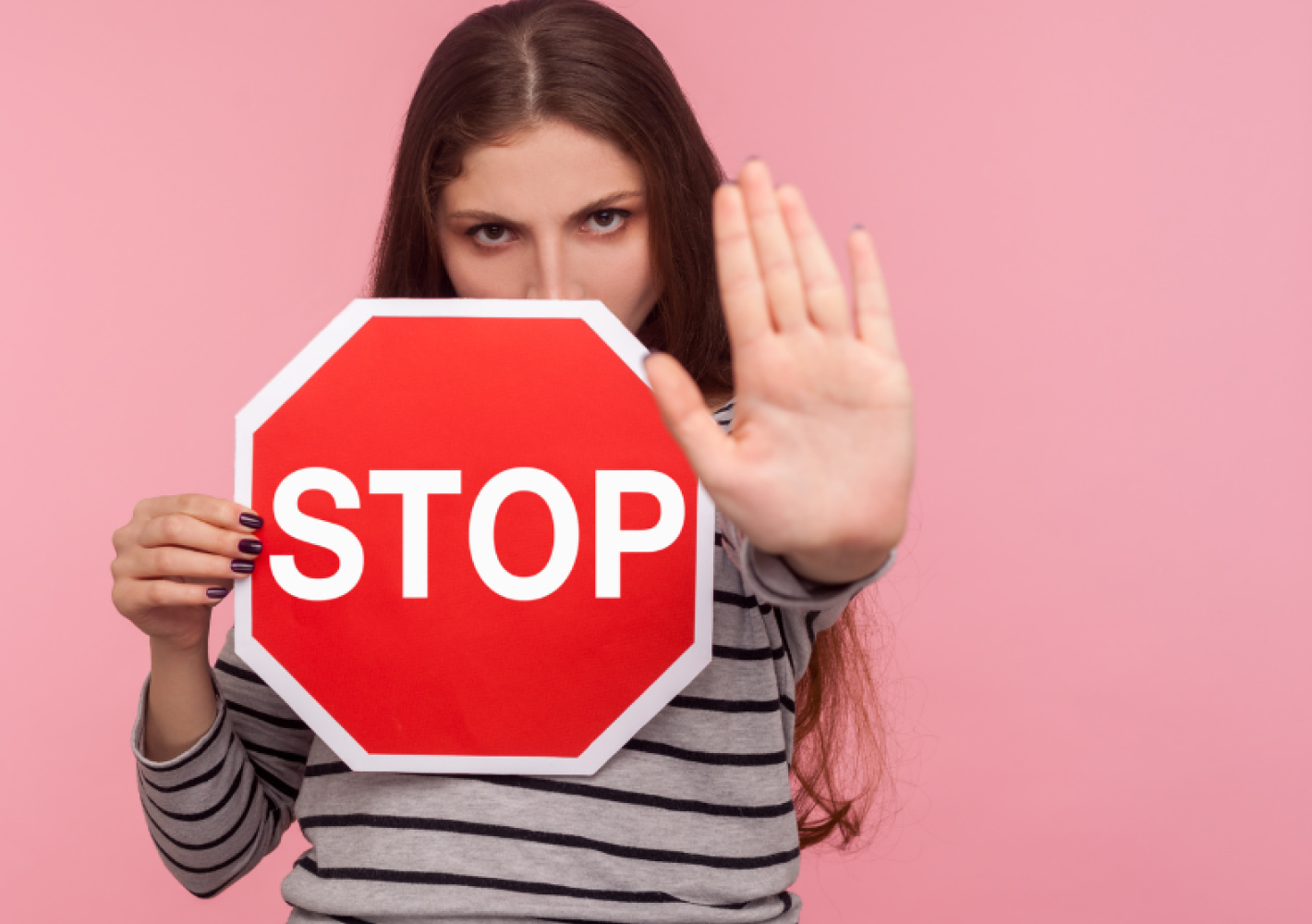 En person holder et rødt stopskilt med teksten 'STOP' og rækker den ene hånd frem i en stopbevægelse mod beskueren